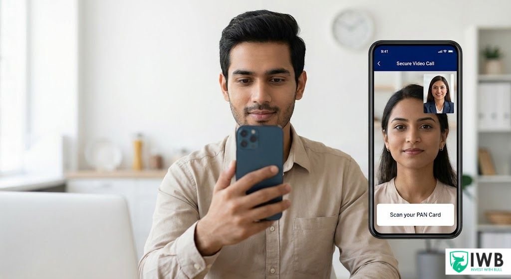 A young Indian professional sitting in a home office, holding a smartphone and looking at the screen which displays a live Video KYC call with an Amex agent and a prompt to scan a PAN card.